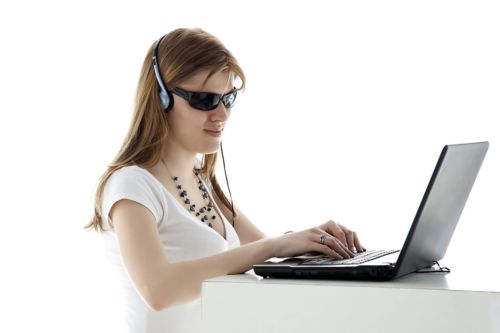На фото молодая девушка за ноутбуком в чёрных очках и наушниках